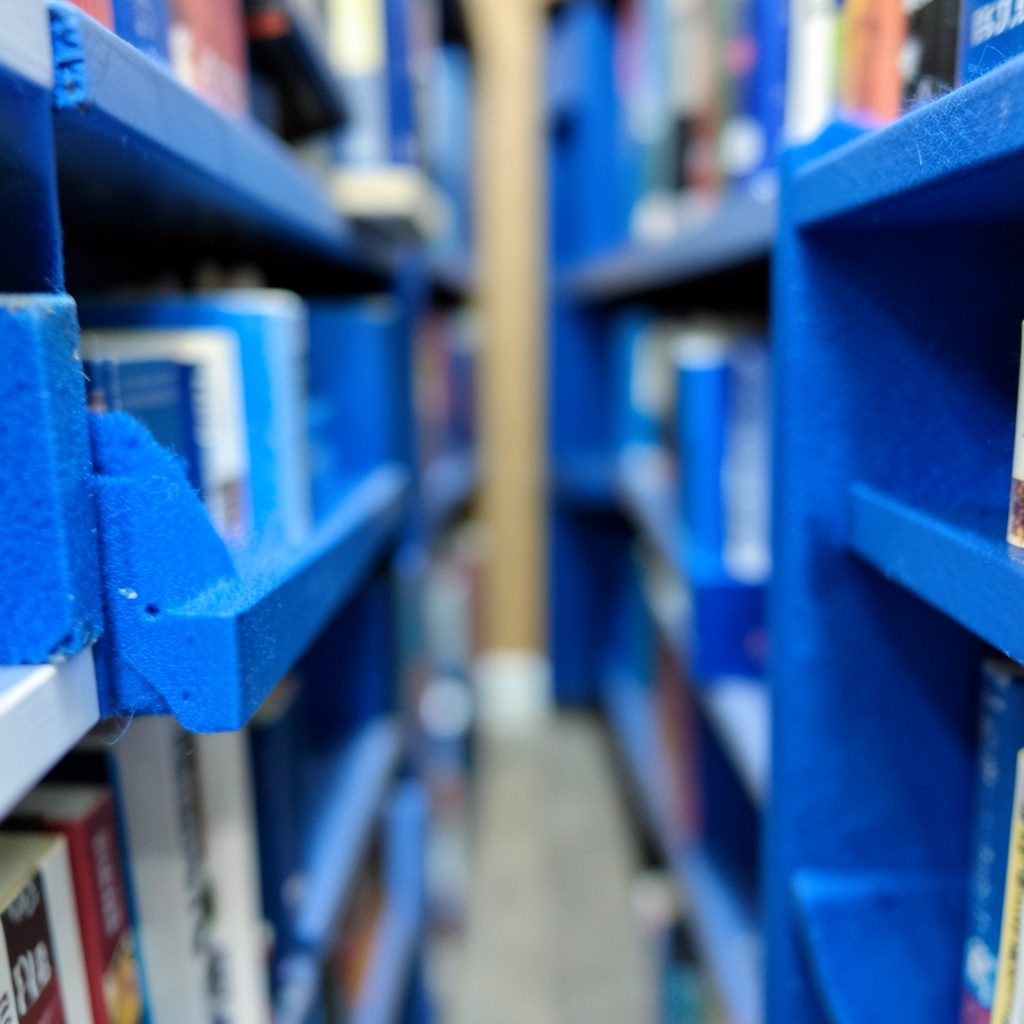 Ett bibliotek i lugna gråblå och beige nyanser med bokhyllor i bakgrunden